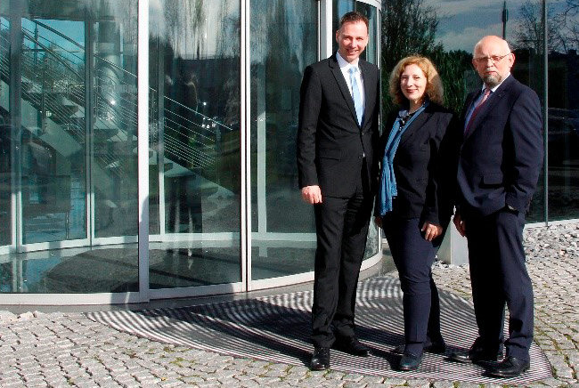 Hendrik Kampmann, Dr. Daniela de Ridder und Hermann Ensink stehen vor dem Eingang des Kampmann Verwaltungsgebäudes und lächeln in die Kamera